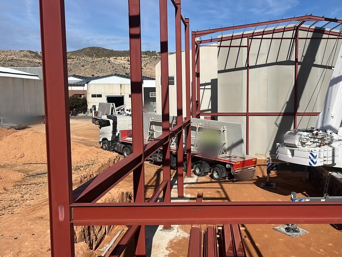 Nave industrial en construcción: estructura metálica, cerramiento de placas de hormigón y camión con las placas